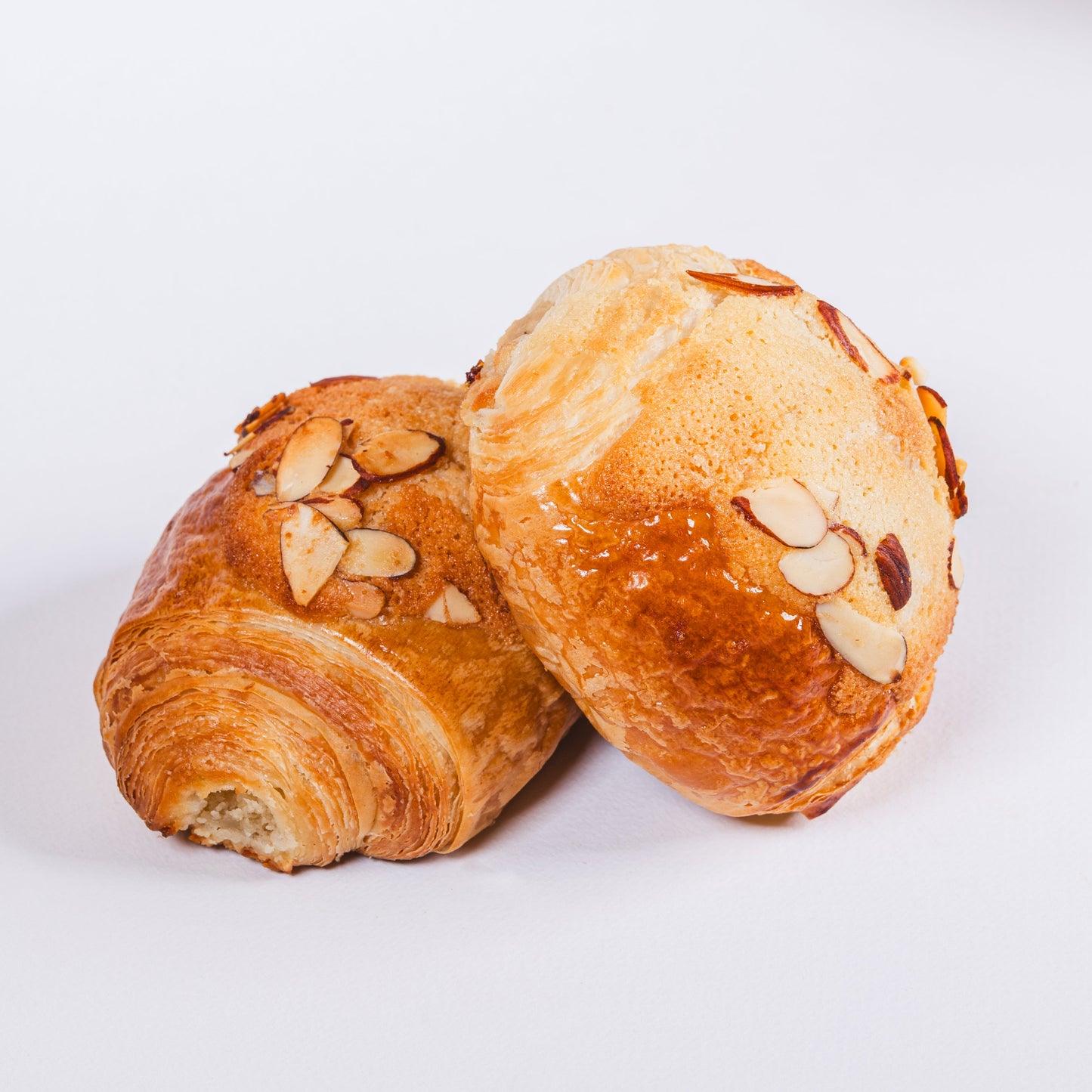 Two golden-brown baked pastries topped with sliced almonds, photographed on a clean white studio background.