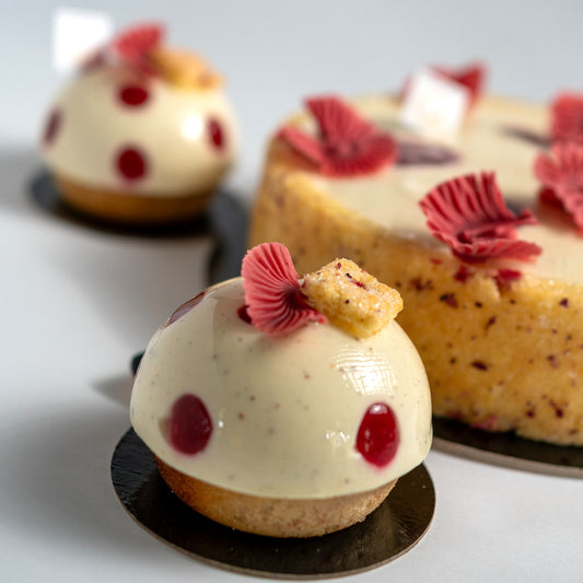 Decorative pastries with white cream, red berries, and pinkberry chocolate decorations on a light background.