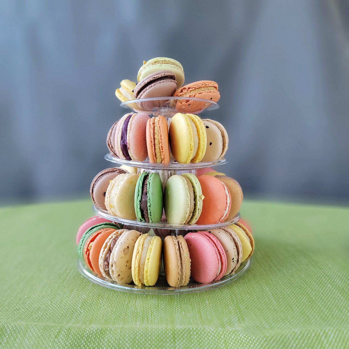 A pyramid-shaped tower of colorful macarons displayed on a clear stand against a grey background with 4 tiers!