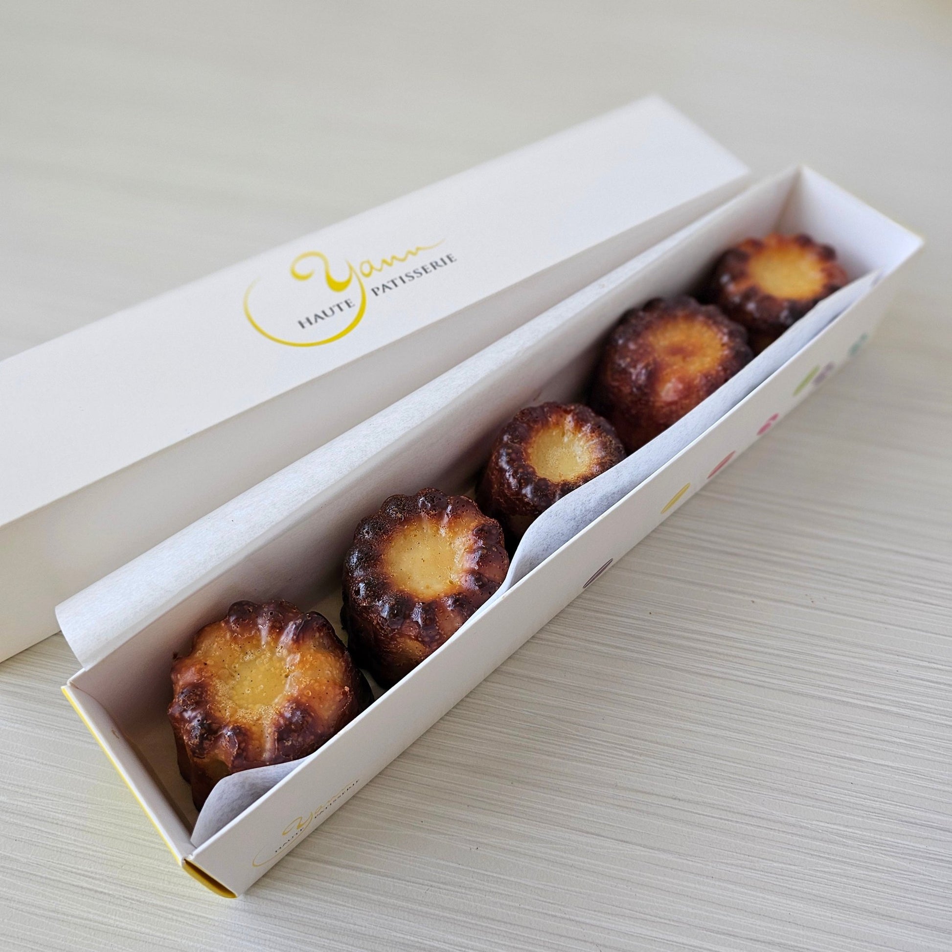 Canneles de Bordeaux in a gift box, vanilla and rum for a unique little treat! Yann Haute Patisserie, French desserts and bakery shop in Calgary. Best pastries like macarons, cakes, birthday cakes, bread, ice cream and almond croissants!