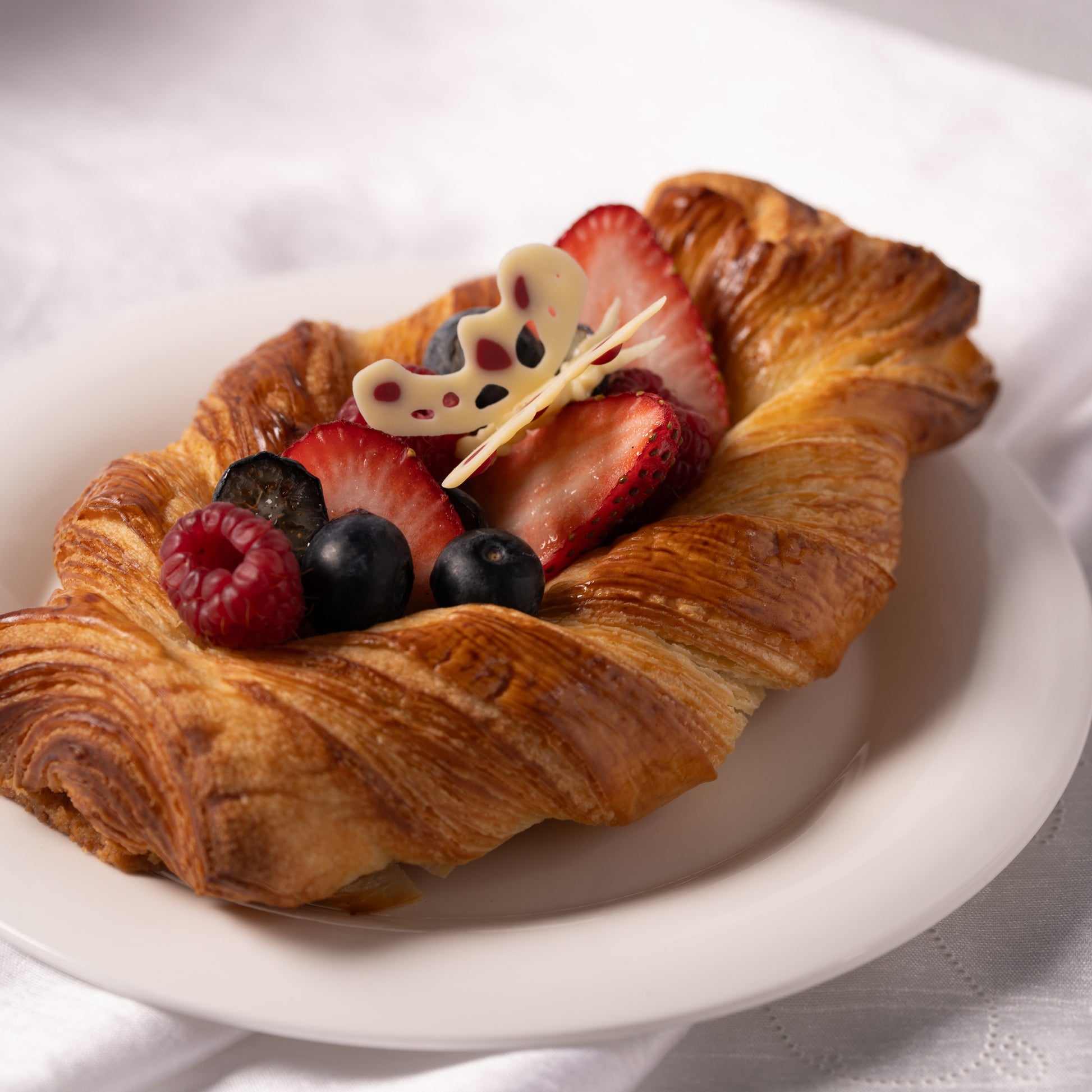 Close-up of fruit croissant with pastry cream and fresh berries, flaky buttery layers with strawberries and blueberries, French bakery Calgary dessert, gourmet croissant texture, handmade pastry YYC, Easter treat Calgary, premium bakery products