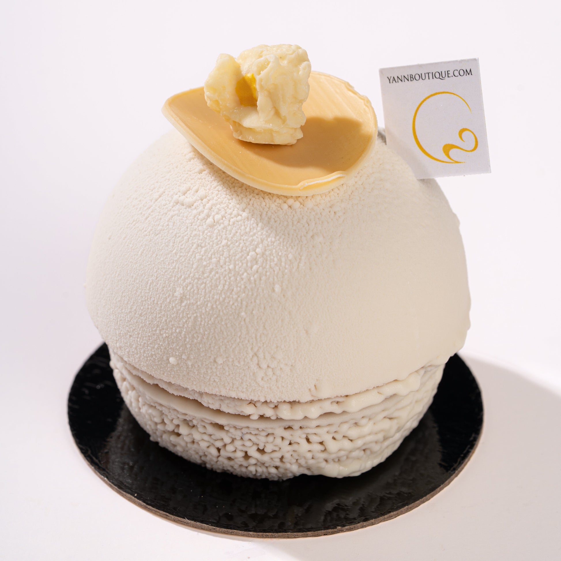 White spherical dessert with a chocolate popcorn on top, placed on a black plate with a white background.