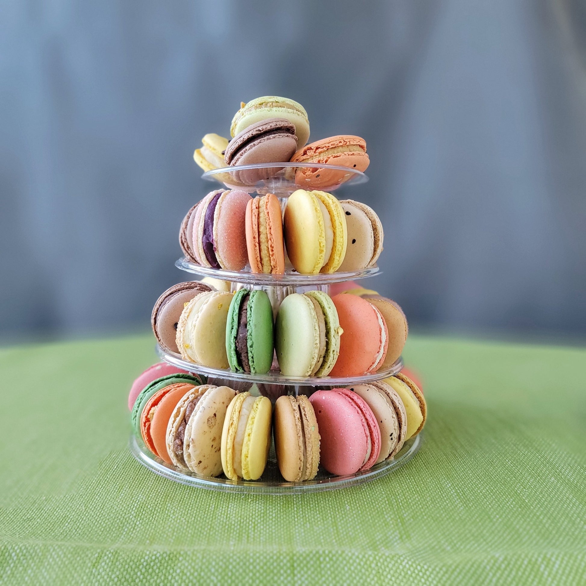 A pyramid-shaped tower of colorful macarons displayed on a clear stand against a grey background with 4 tiers!
