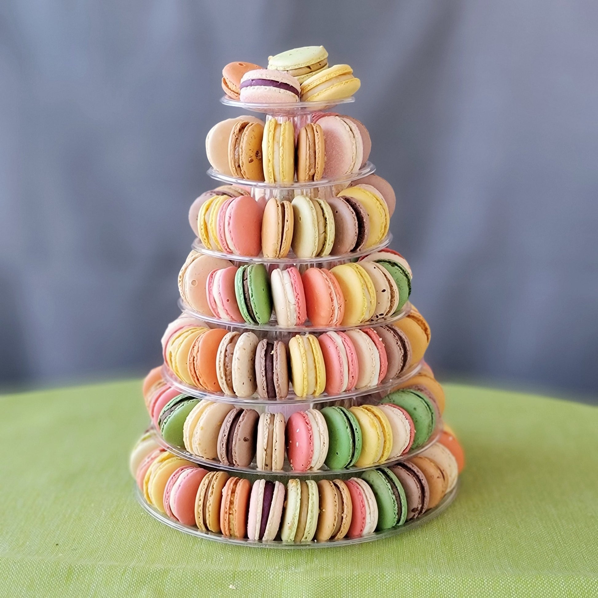 A pyramid-shaped tower of colorful macarons displayed on a clear stand against a grey background with 7 tiers!