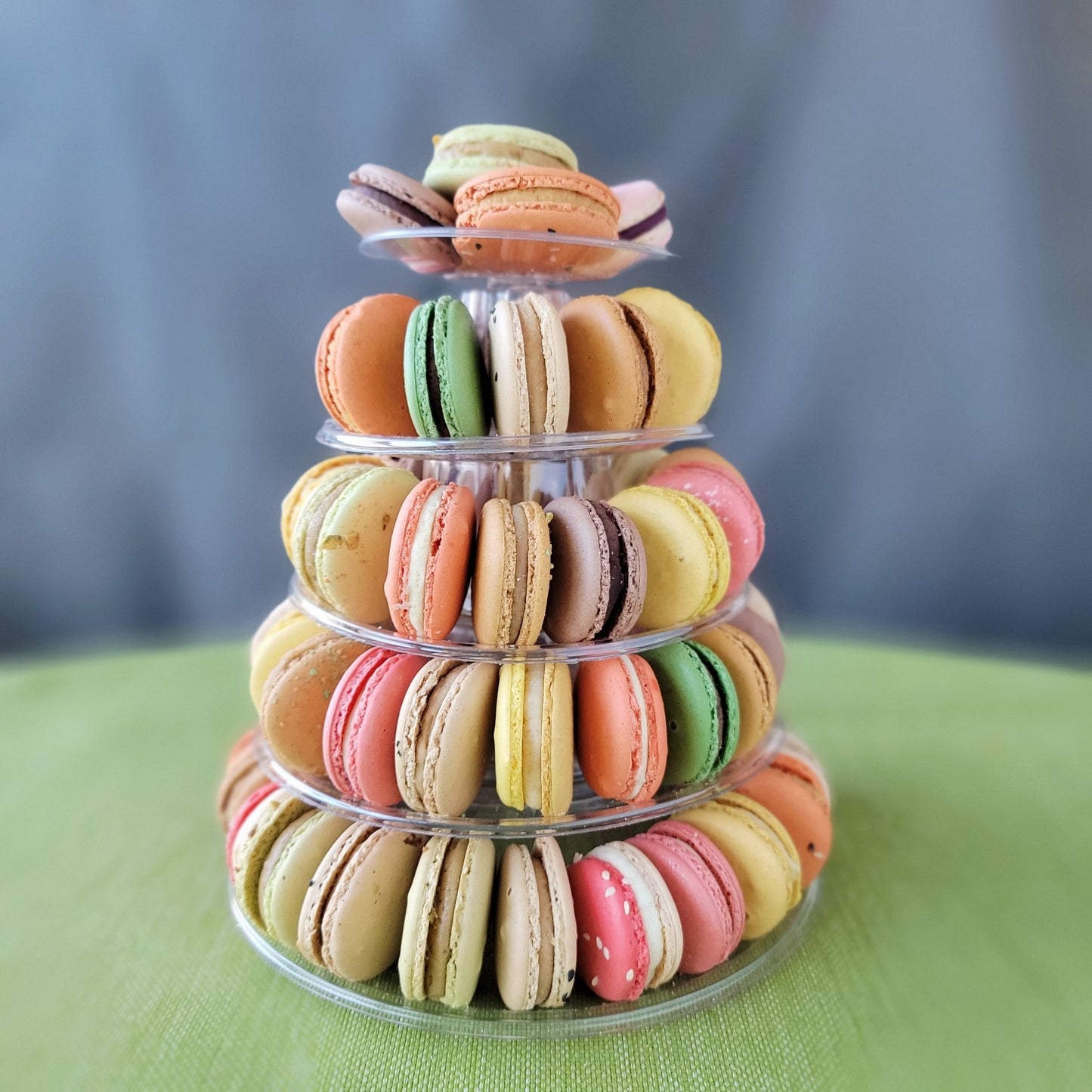 A pyramid-shaped tower of colorful macarons displayed on a clear stand against a grey background with 5 tiers!