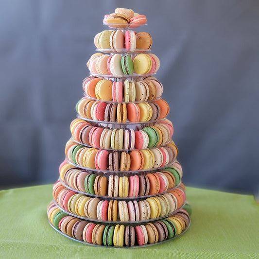 A pyramid-shaped tower of colorful macarons displayed on a clear stand against a grey background with 10 tiers!