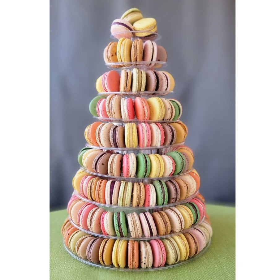 A pyramid-shaped tower of colorful macarons displayed on a clear stand against a grey background with 9 tiers!